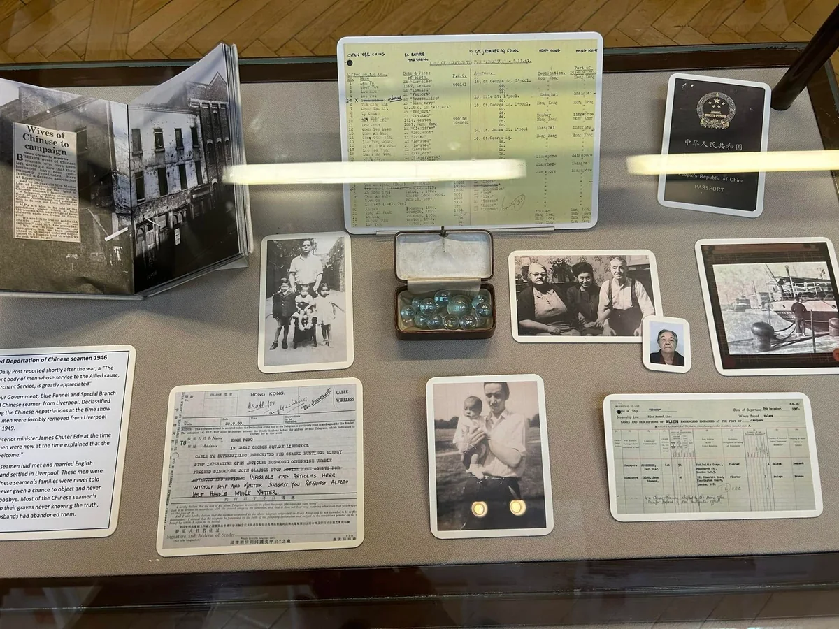 Documents, lists, photographs and small objects arranged in a glass exhibition case.