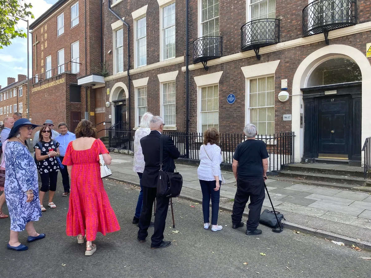 People gathered on the pavement near the memorial plaque.