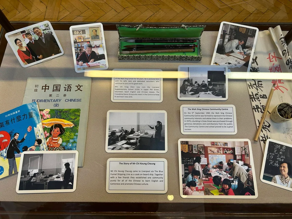Chinese-language textbooks, writing brushes and photographs of classes in an exhibition case.